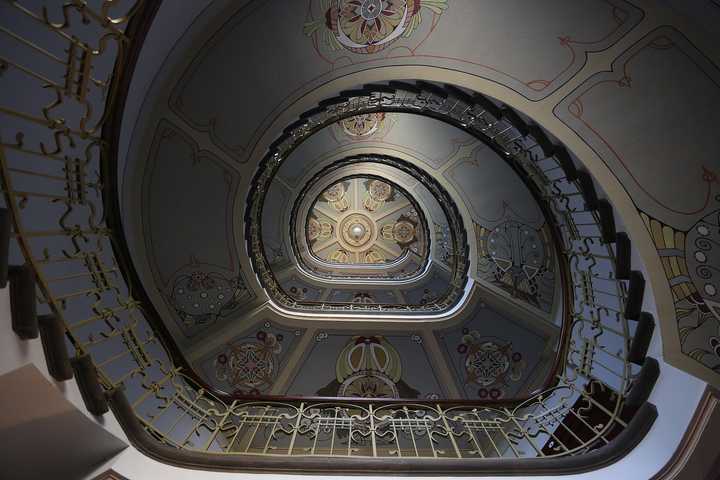 Looking up an oval Art Nouveau staircase with painted ceilings and an ironwork rail.