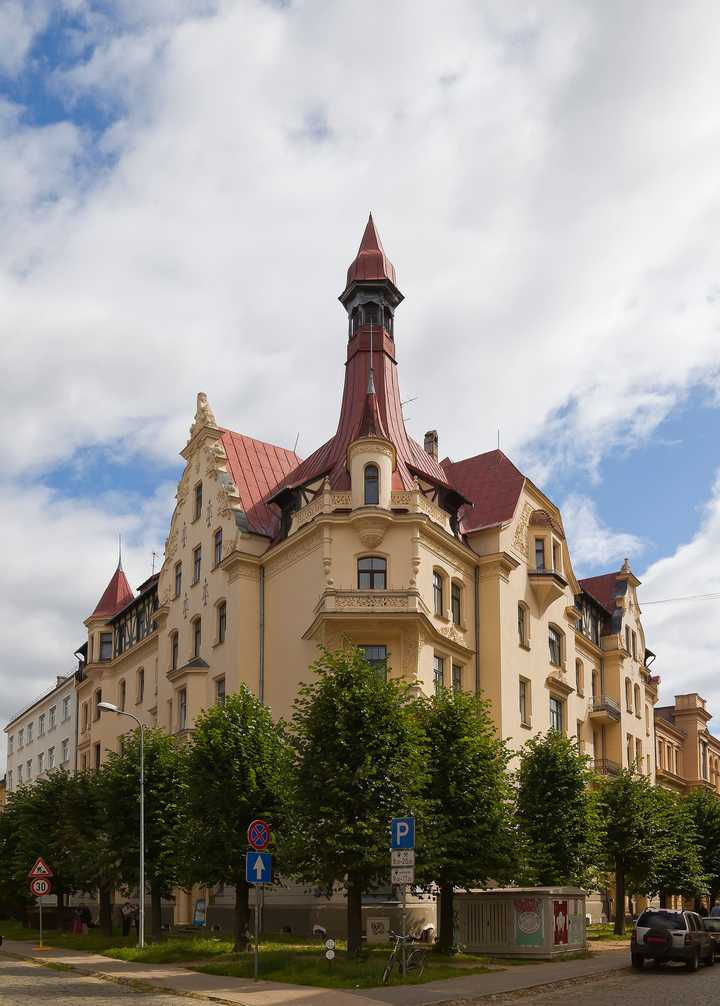 An Art Nouveau corner house with a tall spired turret behind a row of lime trees.